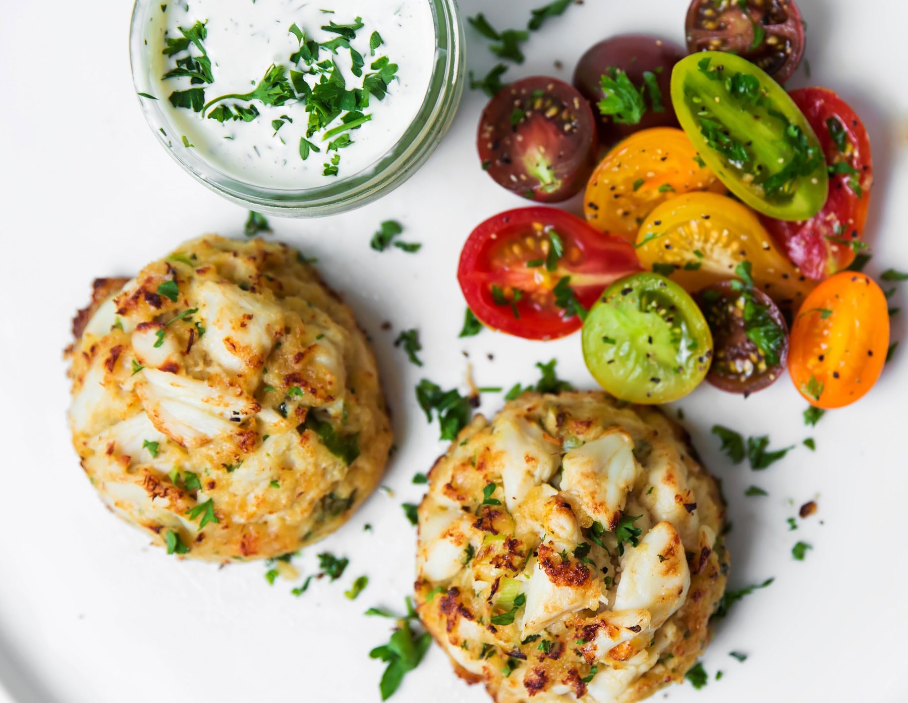 Two golden crab cakes with cherry tomatoes and herb sauce